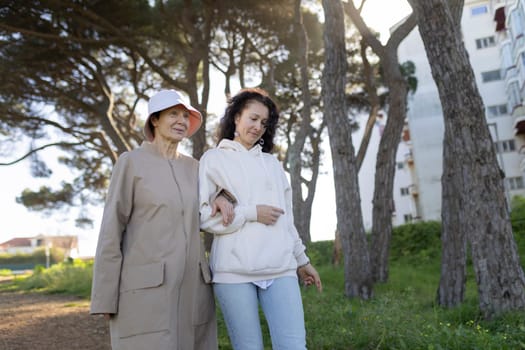 Senior woman and her daughter walking arm in arm in a park, enjoying a sunny day together