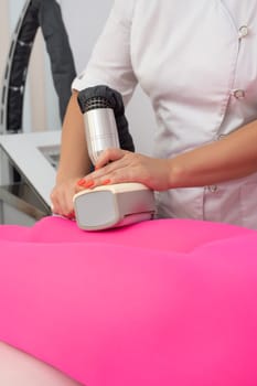 Crop anonymous masseur massaging body of unrecognizable female client in anti cellulite suit with modern apparatus in clinic