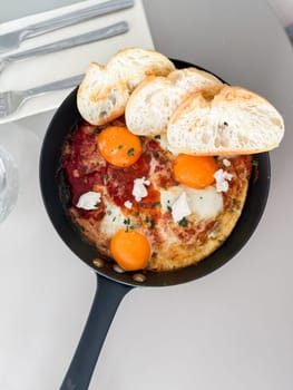 Shakshuka served hot in pan with bread slices. Comfort food, modern brunch and urban culinary style.