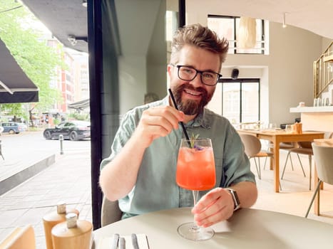 Smiling man over a glass of alcohol cocktail. Joy, relaxation and personal connection through urban drinks.