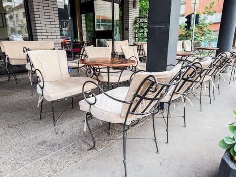 Outdoor cafe terrace with vintage chairs and empty round tables in urban setting. Public leisure and urban coffee culture.