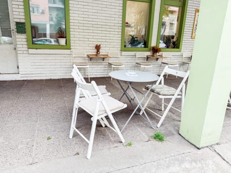 Simple cafe patio with folding white chairs and round metal table against brick wall. Casual street dining and social outdoor space.
