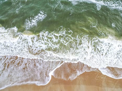 The beach features soft, golden sand that meets clear turquoise waters. Gentle waves lap at the shore, creating a tranquil atmosphere perfect for relaxation and enjoyment.