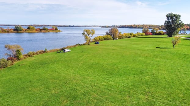 Ottawa, ON Canada - 2024-06-20: Expansive Green Field Surrounded by Peaceful Lake and Beautiful Blue Sky with Clouds.