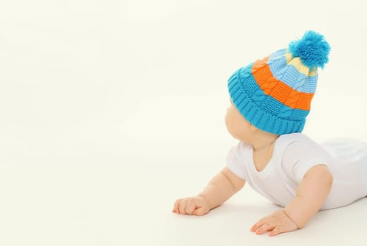 Happy cute baby in winter knitted hat crawling on the floor playing on white studio background