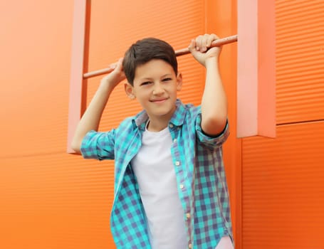Happy smiling teenager boy in casual clothing on city street, orange wall background