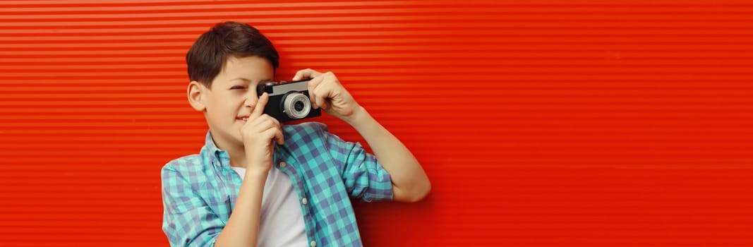 Teenage boy with film camera, kid taking picture standing on bright red background