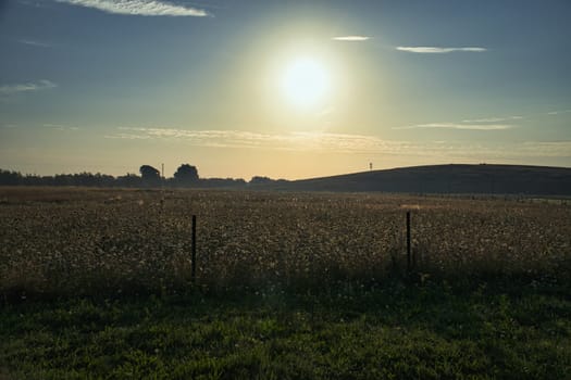 Sunset over a wide field with rolling hills in the background, a wooden fence in the foreground. Warm mood lighting and silhouettes emphasize the landscape.