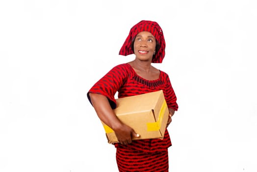beautiful african adult woman wearing red loincloth standing is looking to the side holding a cardboard box and smiling. isolated on white background