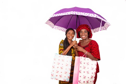 two beautiful business women standing together under a purple umbrella holding a bag in hand while smiling