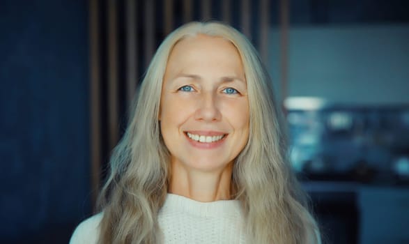 Portrait of beautiful happy smiling mature woman with gray hair looking at camera standing in room at home