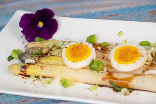 Baked asparagus with boiled egg in big white plate on blue background. High quality photo