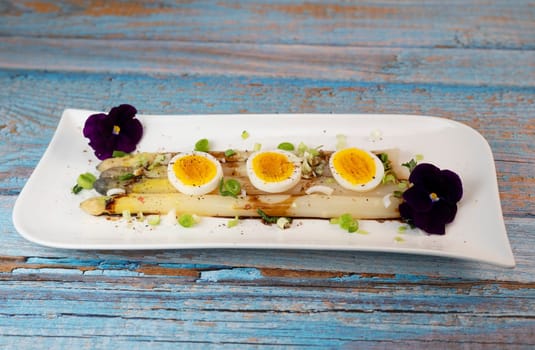 Baked asparagus with boiled egg in big white plate on blue background. High quality photo