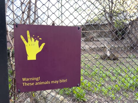 Warning sign on zoo enclosure fence showing bitten hand and message. These animals may bite to caution visitors and promote safety awareness around wild animals