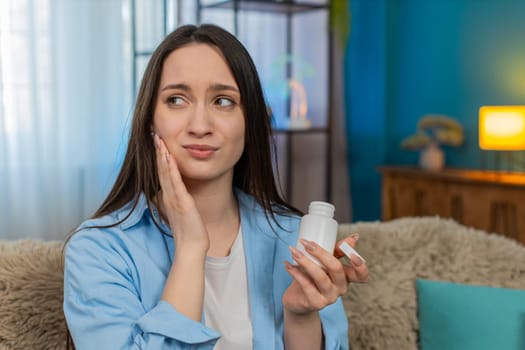 Young ill woman at home suffering from severe toothache, holding cheek painfully, tiredly searching for painkiller pills. Caucasian sick girl experiencing strong discomfort, exhausted by dental pain