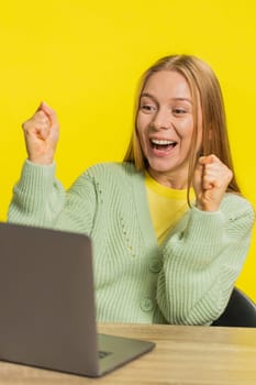Happy Caucasian middle-aged business woman working on laptop netbook shocked by victory celebrate winning goal achievement, good email career news sitting at table isolated on yellow background indoor