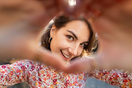 I love you. Caucasian woman makes symbol of love, showing heart sign to camera, express romantic feelings, express sincere positive feelings. Charity, gratitude donation. Outdoors in urban city street