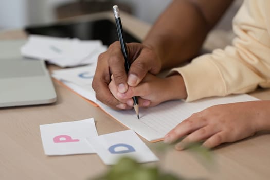 A father assists his son with a writing exercise during their homeschool session, emphasizing collaboration and learning in a homely atmosphere.