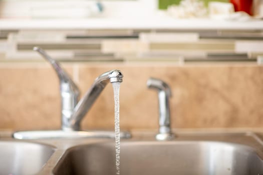 A sink with a faucet that is dripping water. The water is clear and the sink is silver
