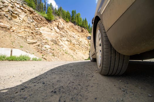 A car is parked on a dirt road next to a rocky hill. The car is dirty and the road is bumpy