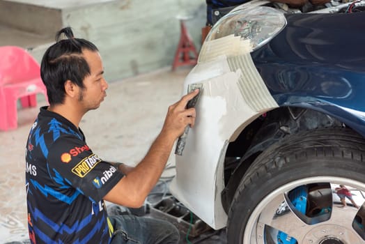 Bangkok, Thailand - April 4, 2024 : Unidentified denter or car mechanic serviceman check and fix body work and fiber bumper body part for fix and repair problem at car garage or repair shop