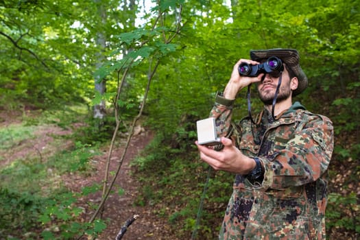 Soldier navigating through dense forest, using binoculars and compass, demonstrating wilderness survival skills