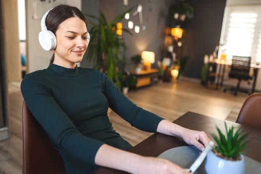 Very happy young girl with white headphones enjoy using a mobile phone indoor.