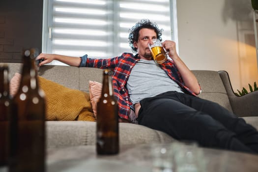 Mid adult man drinking beer at home on sofa, empty bottles around him