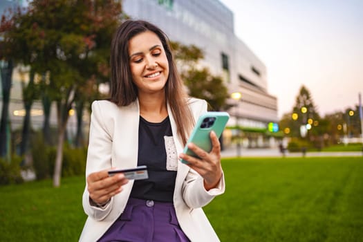 Businesswoman online shopping on a mobile phone at the park after work.