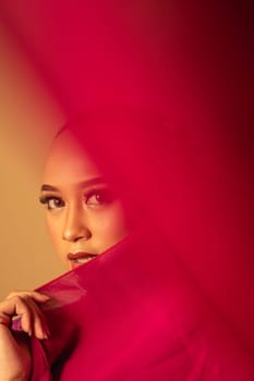 A beautiful Balinese woman covered her makeup face with red fabric from the dress inside the studio
