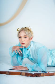 a princess in a blue dress posing on the floor with a bow in a white room