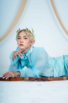 a princess in a blue dress posing on the floor with a bow in a white room