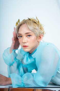 a woman with blonde hair and a blue dress posing with curled arms and a blushing face in front of a white background