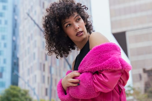Graceful dancer with curly hair wearing a pink coat, expressing movement and energy in an urban environment. Modern fashion, contemporary dance, and artistic performance against a city backdrop.