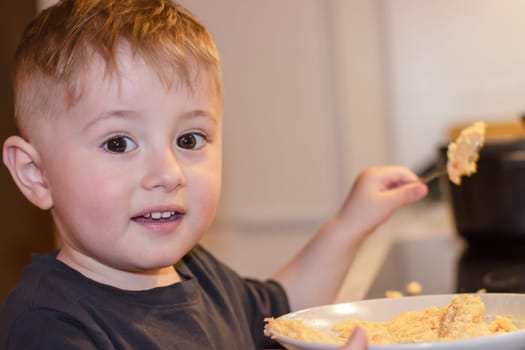 Small child with a spoon eating porridge from a large bowl in the kitchen in the evening. High quality photo