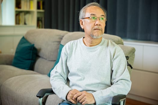 Asian senior man disabled sitting alone on wheelchair in living room looking out window at home and thinking, lonely elder sad old man retirement memory loss or nostalgia thought, feel depressed