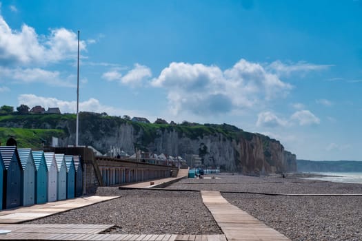 A beach with a row of small blue and white beach houses. The beach is empty and the sky is clear, Dieppe, France