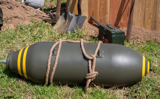 A large bomb is tied to a rope and is laying on the grass. The bomb is surrounded by a pile of dirt and a shovel. The scene is eerie and unsettling, as it suggests a potential danger or threat