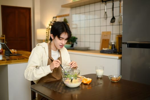 Young Asian man eating healthy breakfast with salad and milk in a kitchen.