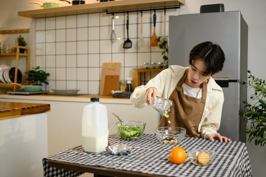 Young man pouring cereal into bowl for breakfast at home kitchen table.