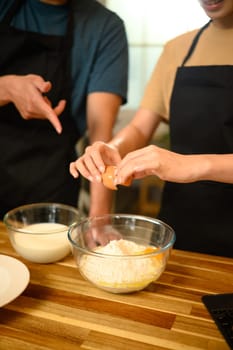 Young couple cracking egg into flour while preparing pancake batter together.
