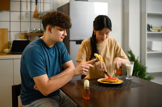 Happy couple enjoying homemade pancakes together at breakfast table.