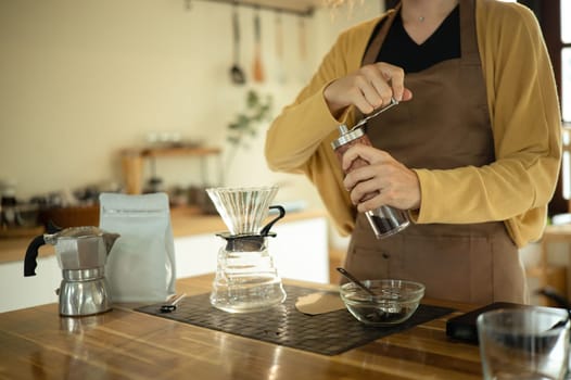 Young woman grinding coffee beans by hand in a kitchen preparing for fresh pour over brew.