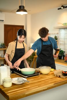 Man and woman in aprons starting to make pancakes in cozy home kitchen.