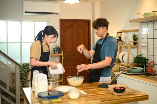 Young couple preparing pancake ingredients together in cozy kitchen.