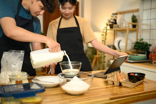 Young couple cooking breakfast and following recipe instructions on digital device.