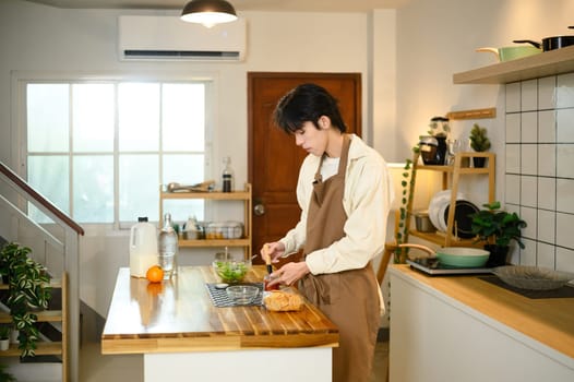 Young asian man preparing healthy vegetable salad in modern kitchen.