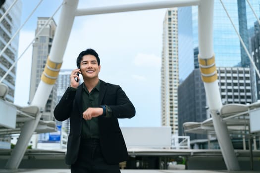 Confident businessman checking time on smartwatch, standing in a modern city.