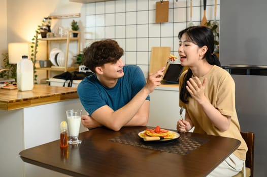 Happy couple enjoying homemade pancakes together at breakfast table.