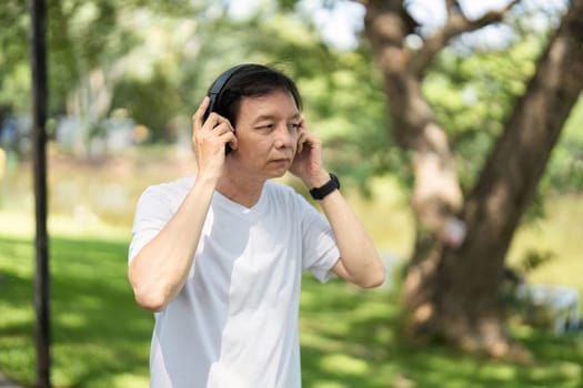 An elderly man adjusts his headphones, immersed in music while enjoying a peaceful outdoor setting, promoting wellness.